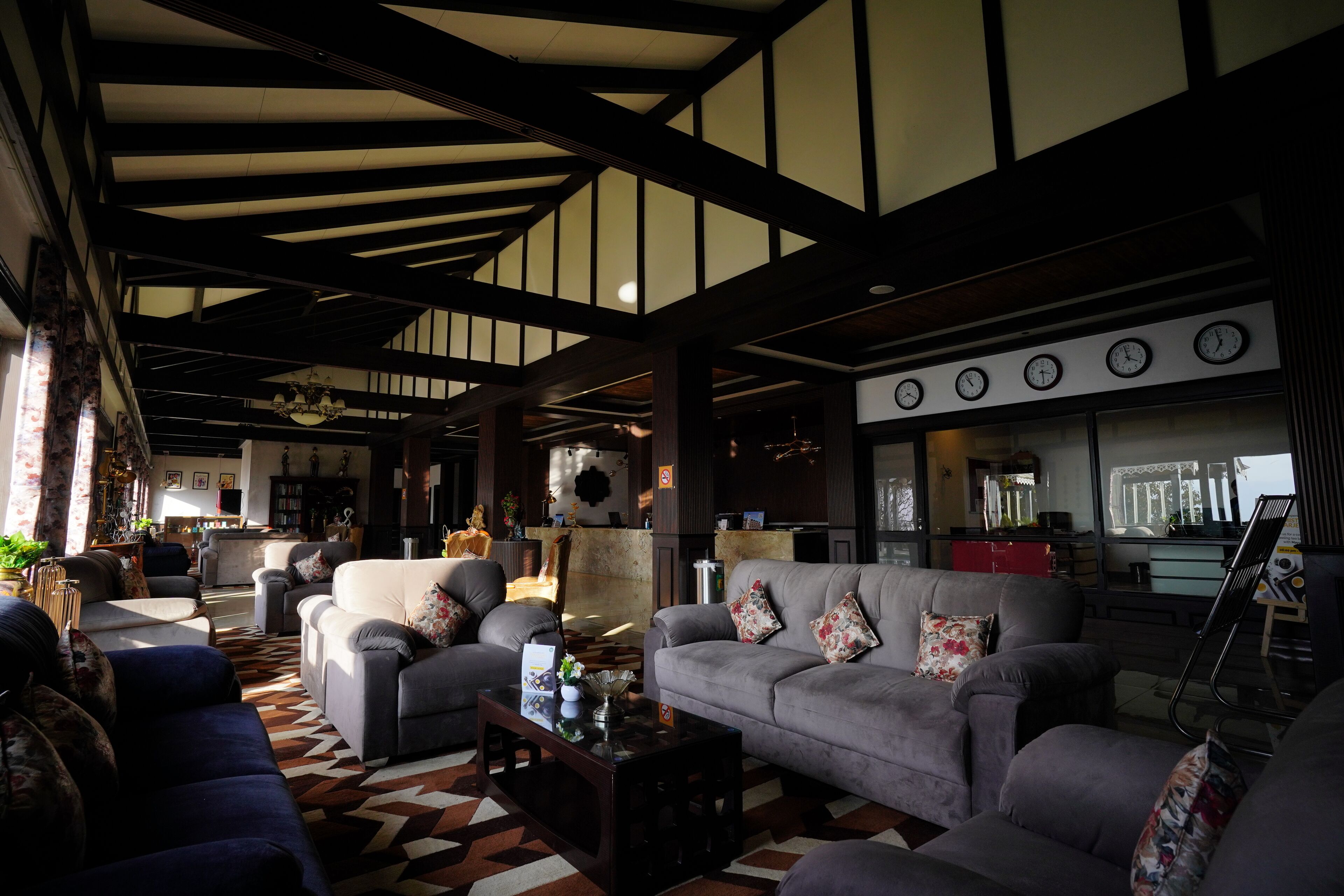 A spacious living room with a high ceiling, multiple sofas, a coffee table, and a large window with clocks.