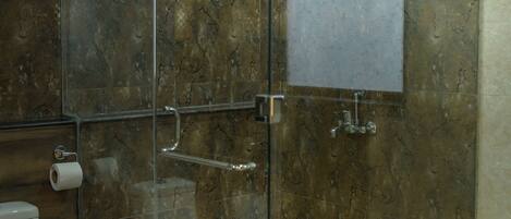 Une cabine de douche fermée par des parois de verre, avec un mur en marbre, des toilettes et un seau rouge.