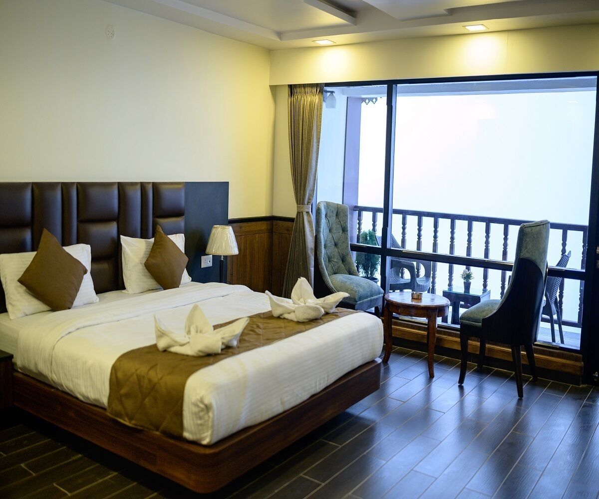 A hotel room with a large bed, a balcony with chairs, and a view of the outside.