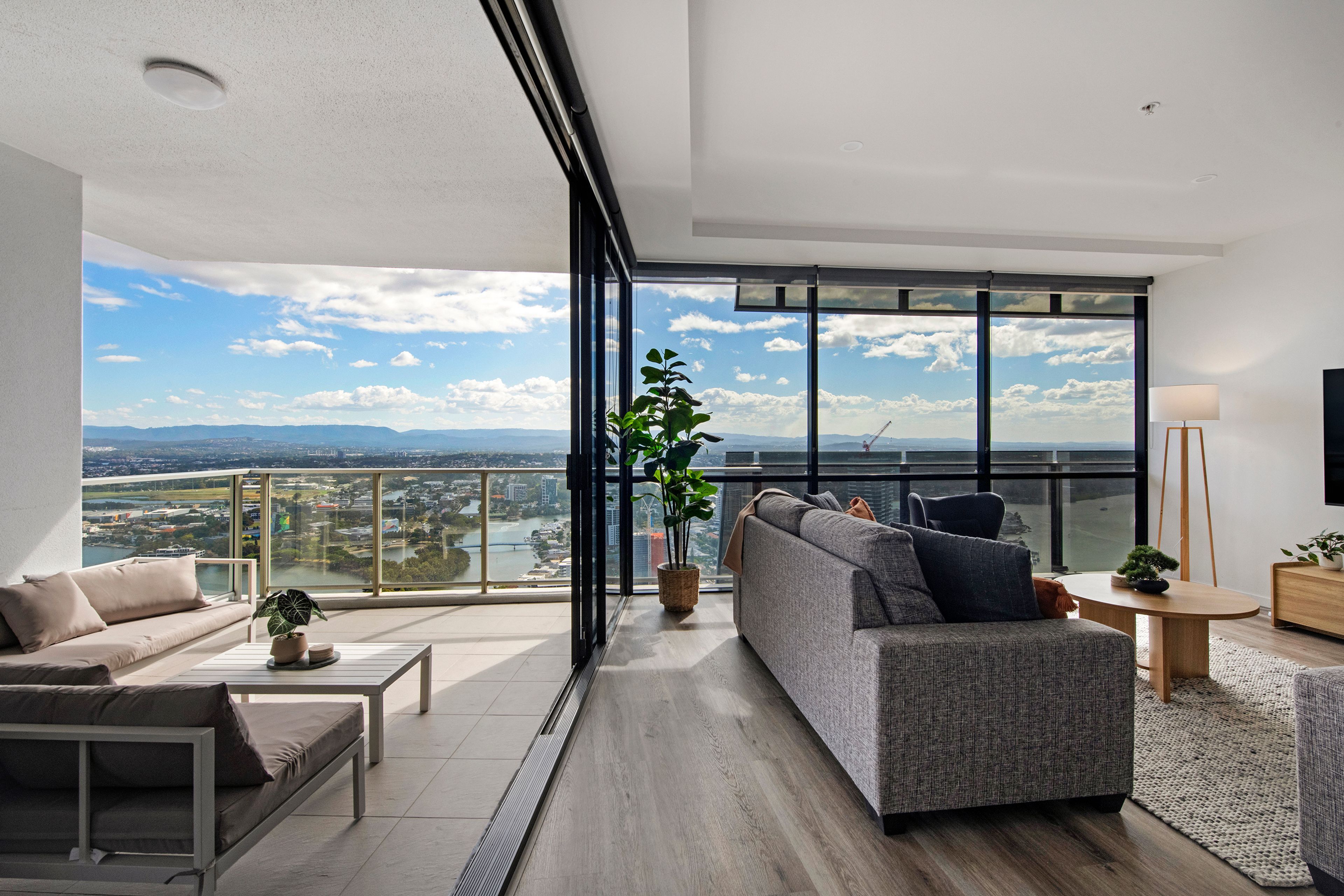 A modern living room with a large window, a sofa, a coffee table, and a potted plant.