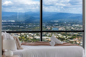 A bedroom with a large window offering a view of a cityscape and mountains.