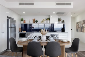 Une cuisine moderne avec un coin repas, comprenant un grand îlot central, des meubles blancs et une vue sur les montagnes.