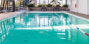 En indendørs swimmingpool med klart vand, et springbræt og liggestole.