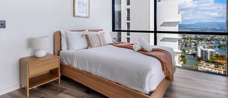 Un dormitorio moderno con un ventanal grande, una cama con ropa blanca, una mesita de noche y un cuadro enmarcado en la pared.