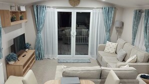 A modern living room with a wooden dining table, a sofa, and a TV. - Impeccable 3-bed Caravan in Clacton-on-sea (Clacton-on-Sea)