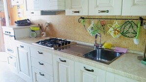 Een keuken met witte kastjes, een gasfornuis, een roestvrijstalen spoelbak en een betegelde spatwand.
