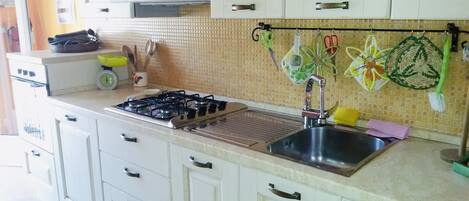 Una cocina con armarios blancos, estufa a gas, pileta de acero inoxidable y salpicadero de azulejos.