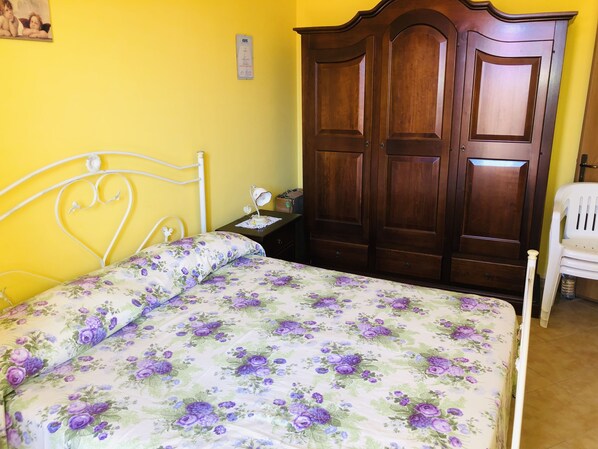 A bedroom with a bed, a wooden wardrobe, a nightstand, and a white chair.