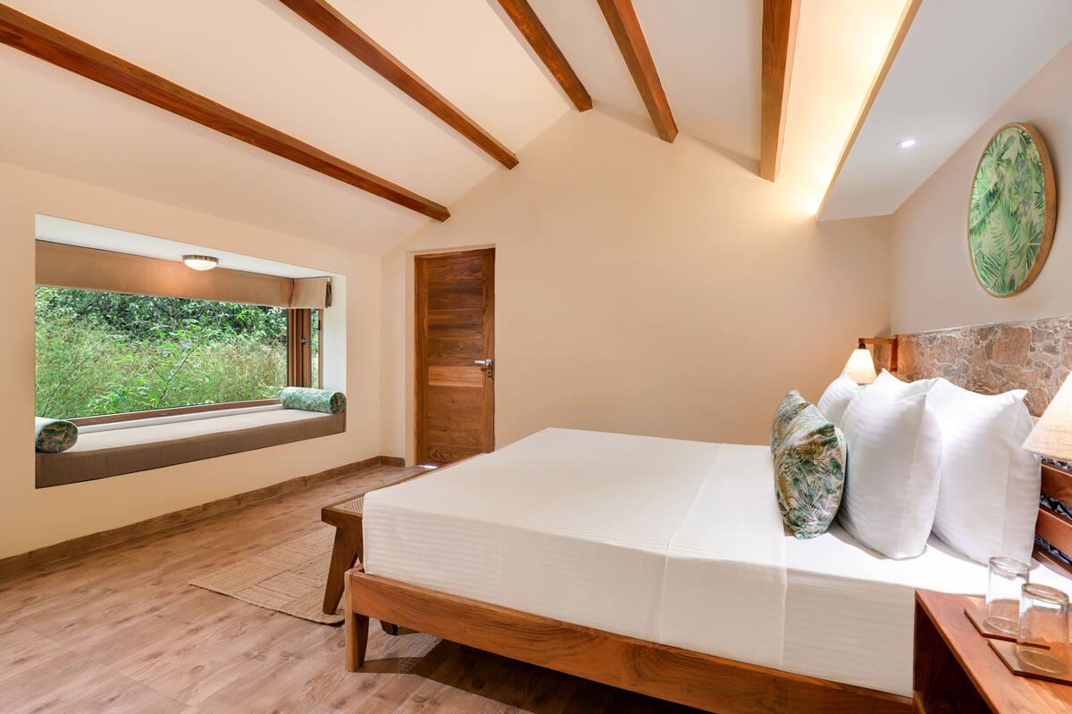 A bedroom with a wooden bed, a window seat, a stone accent wall, and a view of greenery.