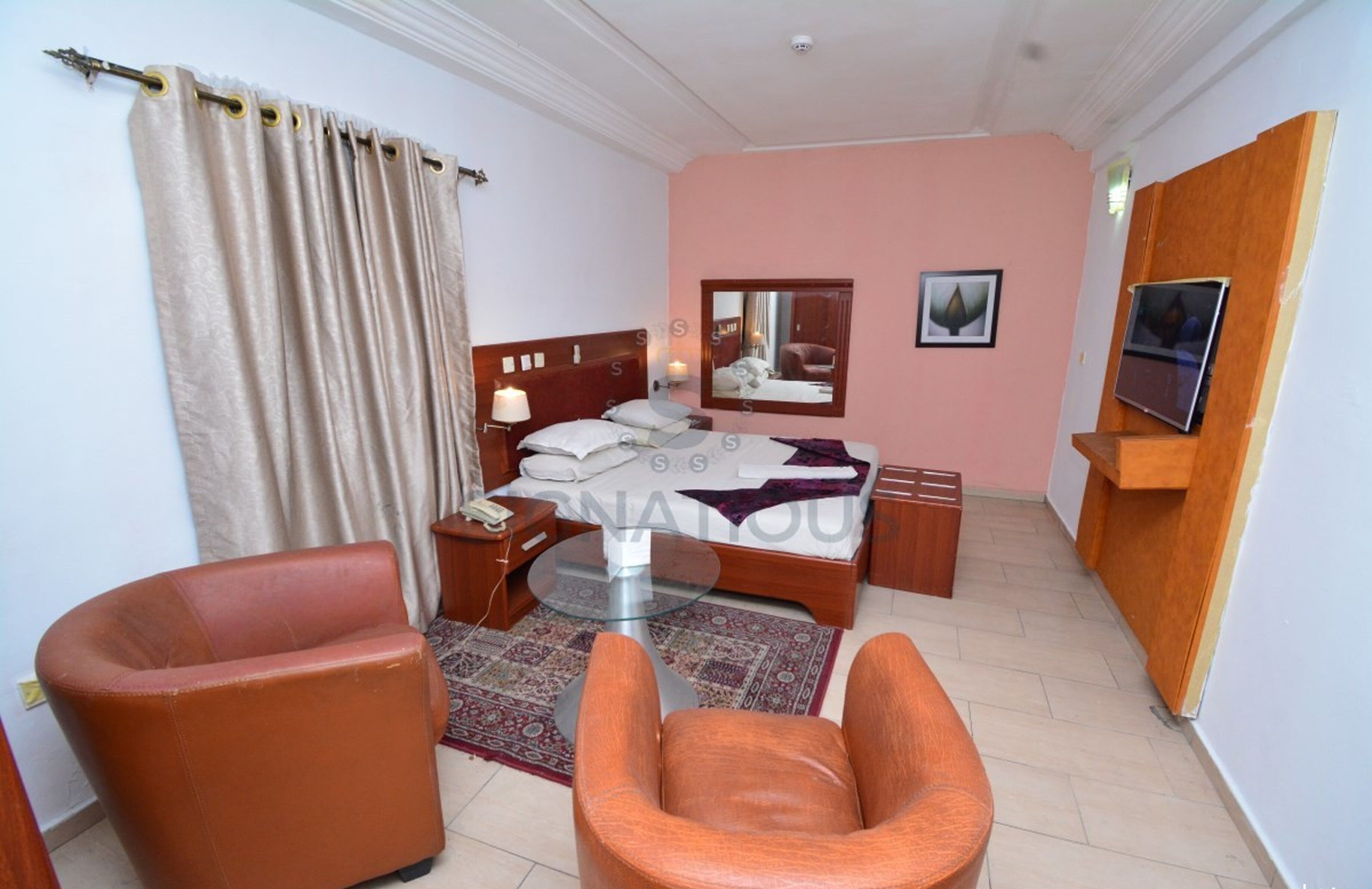 A hotel room with a bed, two chairs, a small table, a mirror, and a TV.