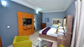 A hotel room with a bed, a TV mounted on the wall, a small table, and two chairs. - Signatious Hotel and Suites (Warri)