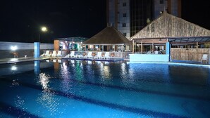 A swimming pool with lounge chairs and a covered area, surrounded by a high-rise building.