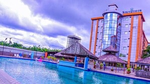 Un hotel con piscina, una estructura de techo de paja y un edificio alto con el letrero "SIGNATIOUS".