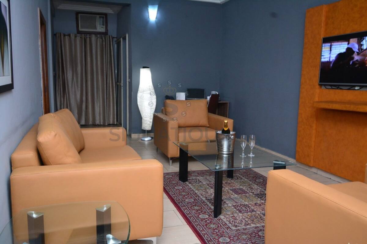 A living room with a sofa, a glass coffee table, a TV mounted on the wall, and a patterned rug.