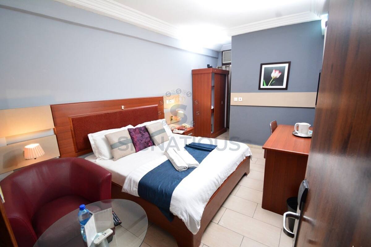A hotel room with a bed, a desk, a chair, a lamp, and a picture on the wall.