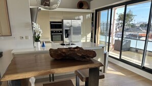 Eine moderne Küche mit Esstisch aus Holz, Edelstahlgeräten und einem großen Fenster mit Blick auf die Stadt.