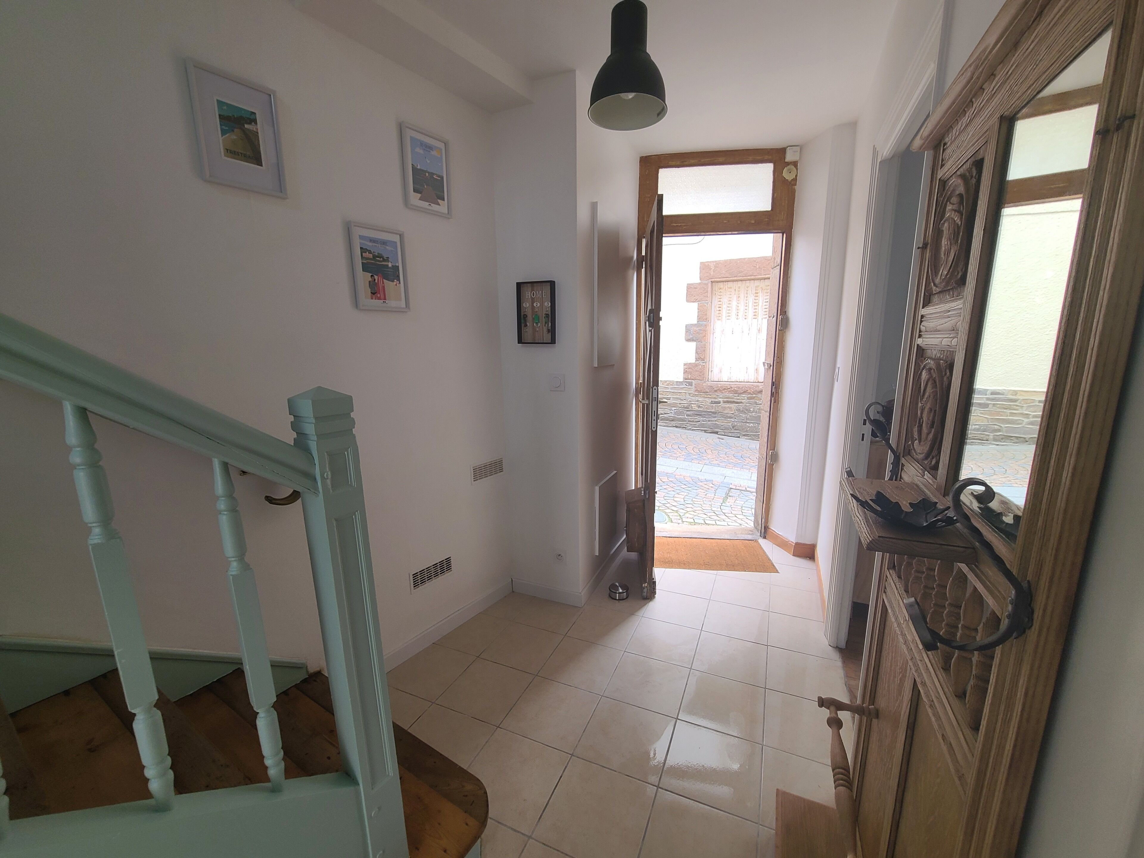 A hallway with a wooden staircase, a door leading outside, and a tiled floor.