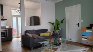 Un salon avec un canapé, une table basse et une plante. On aperçoit une porte et un meuble en arrière-plan.