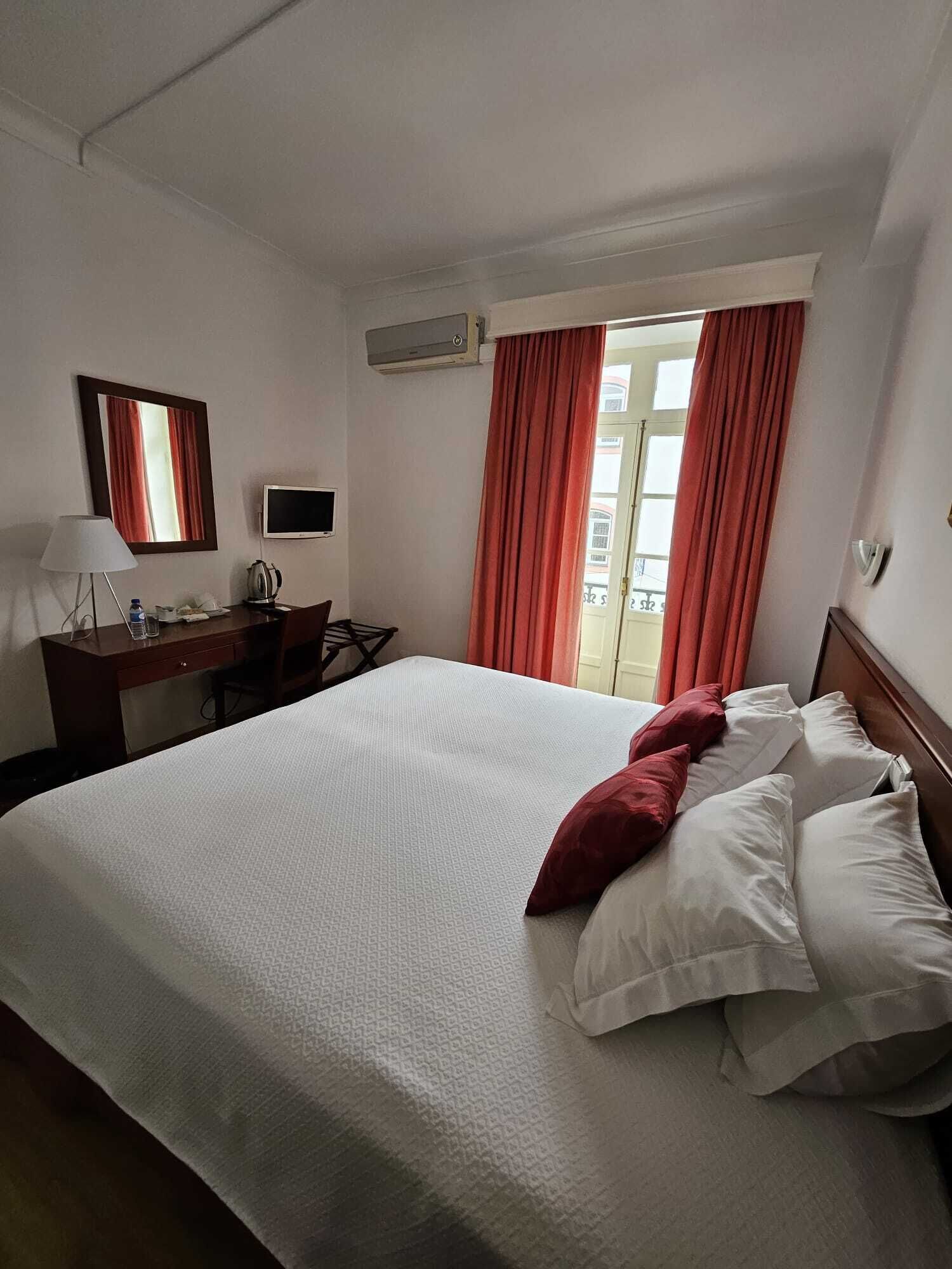 Una camera d'albergo con un letto, una scrivania con un computer, una lampada e un condizionatore d'aria.