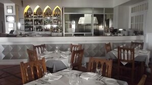 Un restaurante con mesas listas para comer, una zona de bar con botellas y una cocina visible a través del ventanal.