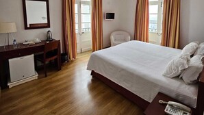 Habitación de hotel con cama, escritorio con silla, pequeña mesa con teléfono y televisor en la pared.