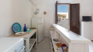 A compact kitchen with a white refrigerator, a small table with dishes, and a TV on a cabinet. - 3681 Casakore by Barbarhouse (Porto Cesareo)