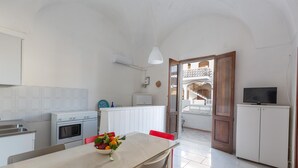 A modern kitchen with white cabinets, a dining table with red chairs, a bowl of fruit, and a TV on a cabinet. - 3681 Casakore by Barbarhouse (Porto Cesareo)