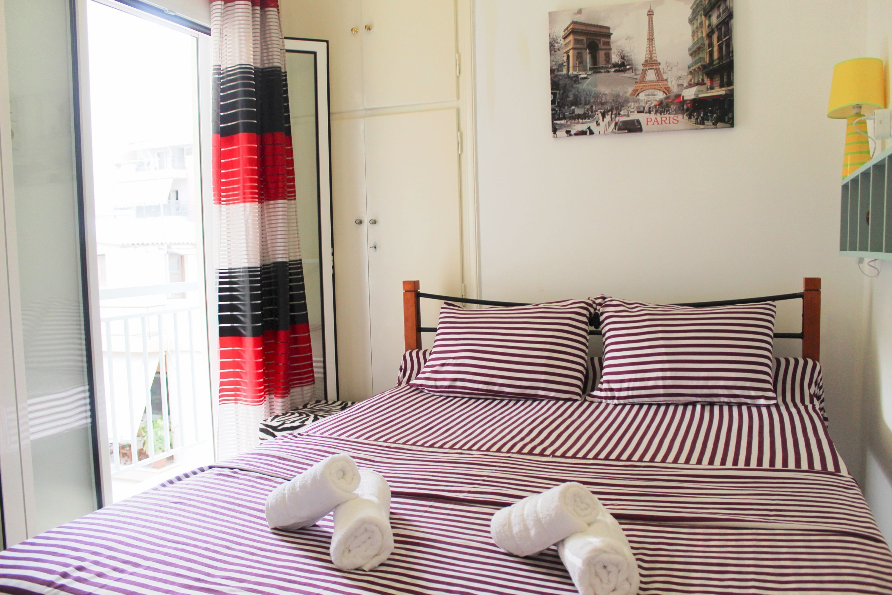 Une chambre d’hôtel avec un lit doté de draps à rayures, une vue sur la Tour Eiffel et une porte donnant sur un balcon extérieur.