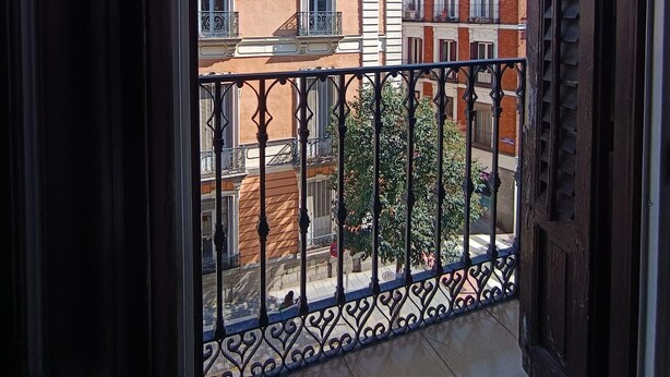 A balcony with a wrought iron railing, a tiled floor, and a view of buildings with red and white facades. - Flat55madrid (Madrid)