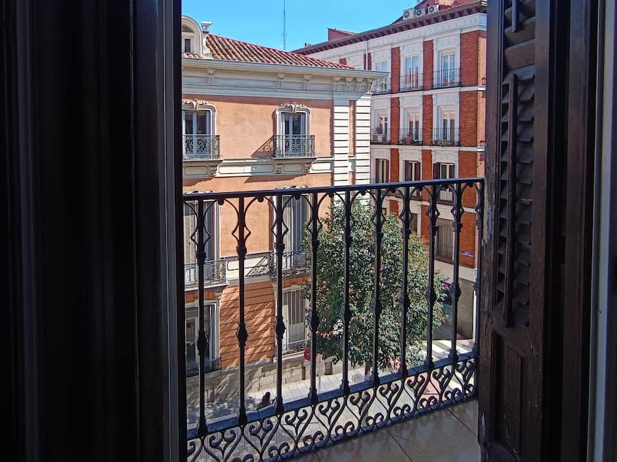 Un balcon doté d’une balustrade en fer forgé, d’un sol carrelé et offrant une vue sur des immeubles aux façades rouges et blanches.