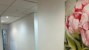 A hallway with wooden flooring and white walls, leading to a room with a large painting of pink flowers. - Flat55madrid (Madrid)