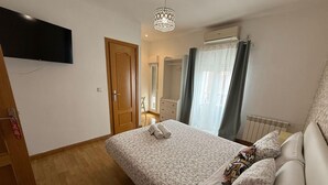 A bedroom with a bed, a television mounted on the wall, a door, and a window with curtains. - Flat55madrid (Madrid)