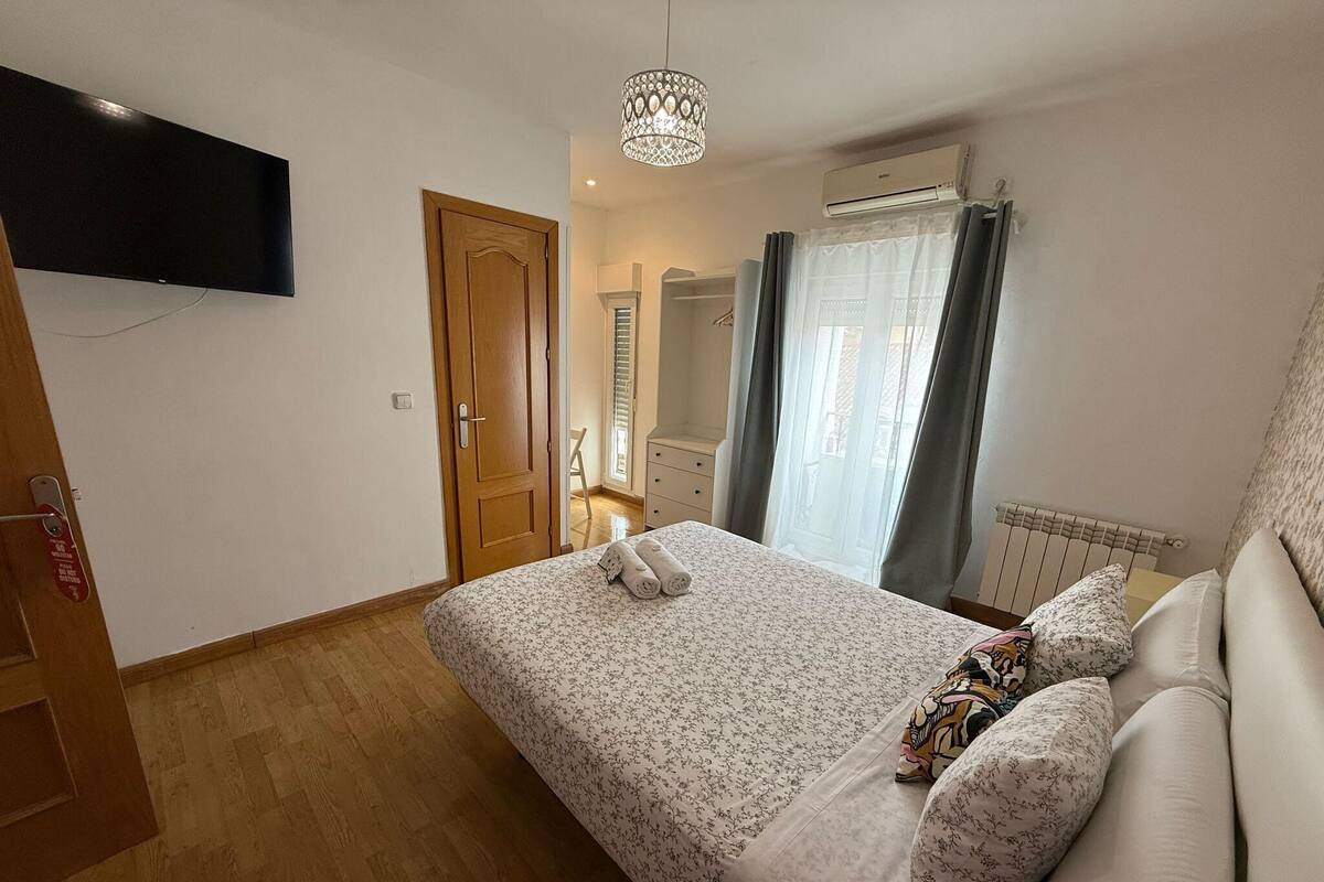 A bedroom with a bed, a television mounted on the wall, a door, and a window with curtains.