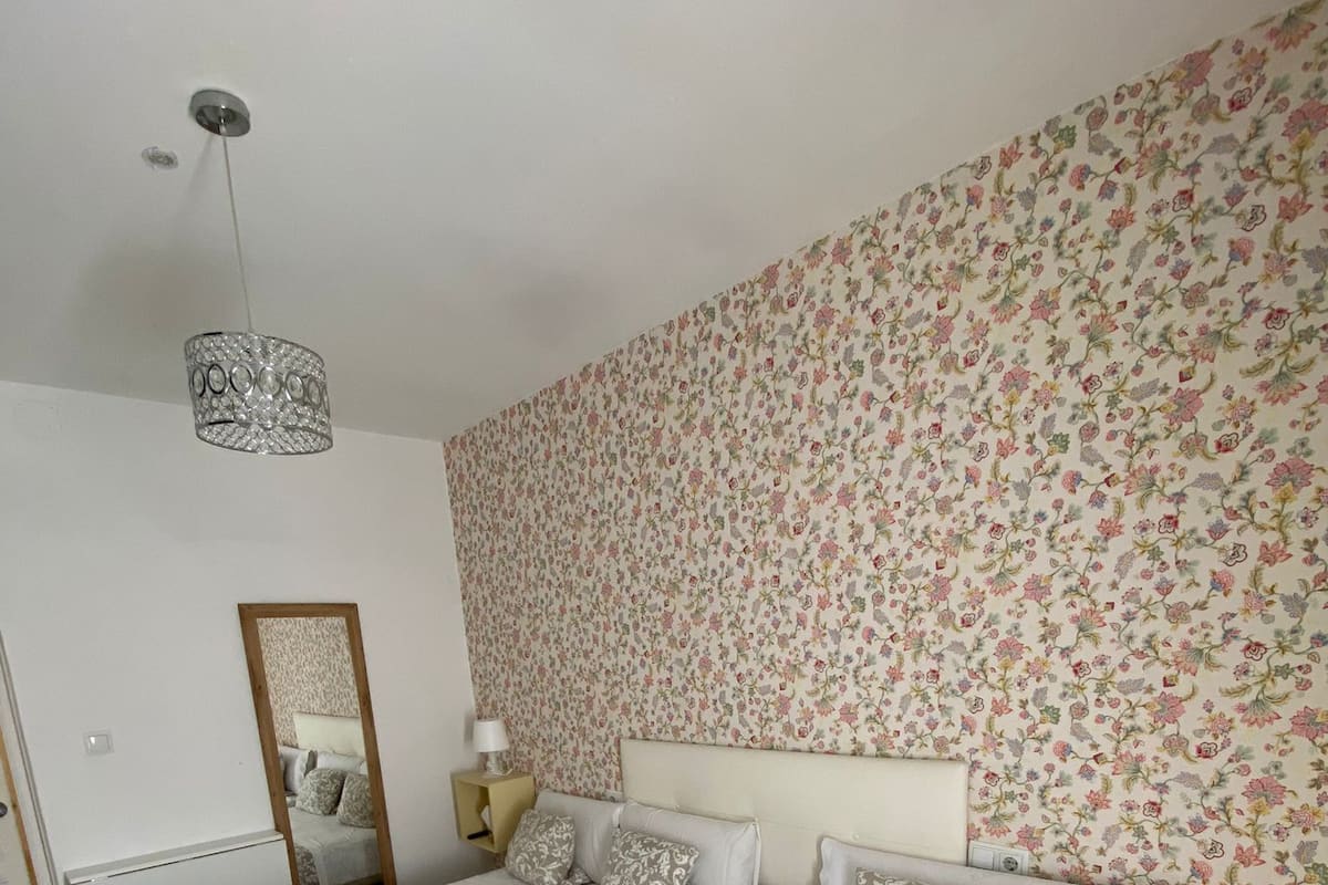 A hotel room with two beds, floral wallpaper, a chandelier, a mirror, and a wooden floor.
