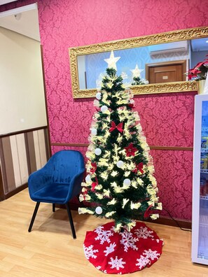 Een kerstboom met witte en rode decoraties, een blauwe stoel en een rood tapijt met sneeuwvlokken.