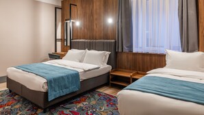 Una habitación de hotel moderna con dos camas, un cabecero de madera, una mesita de noche de madera pequeña y una alfombra colorida con estampado.