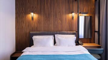Ein Hotelzimmer mit einem hölzernen Kopfteil, zwei Nachttischlampen, einem Telefontisch und einem großen Spiegel.