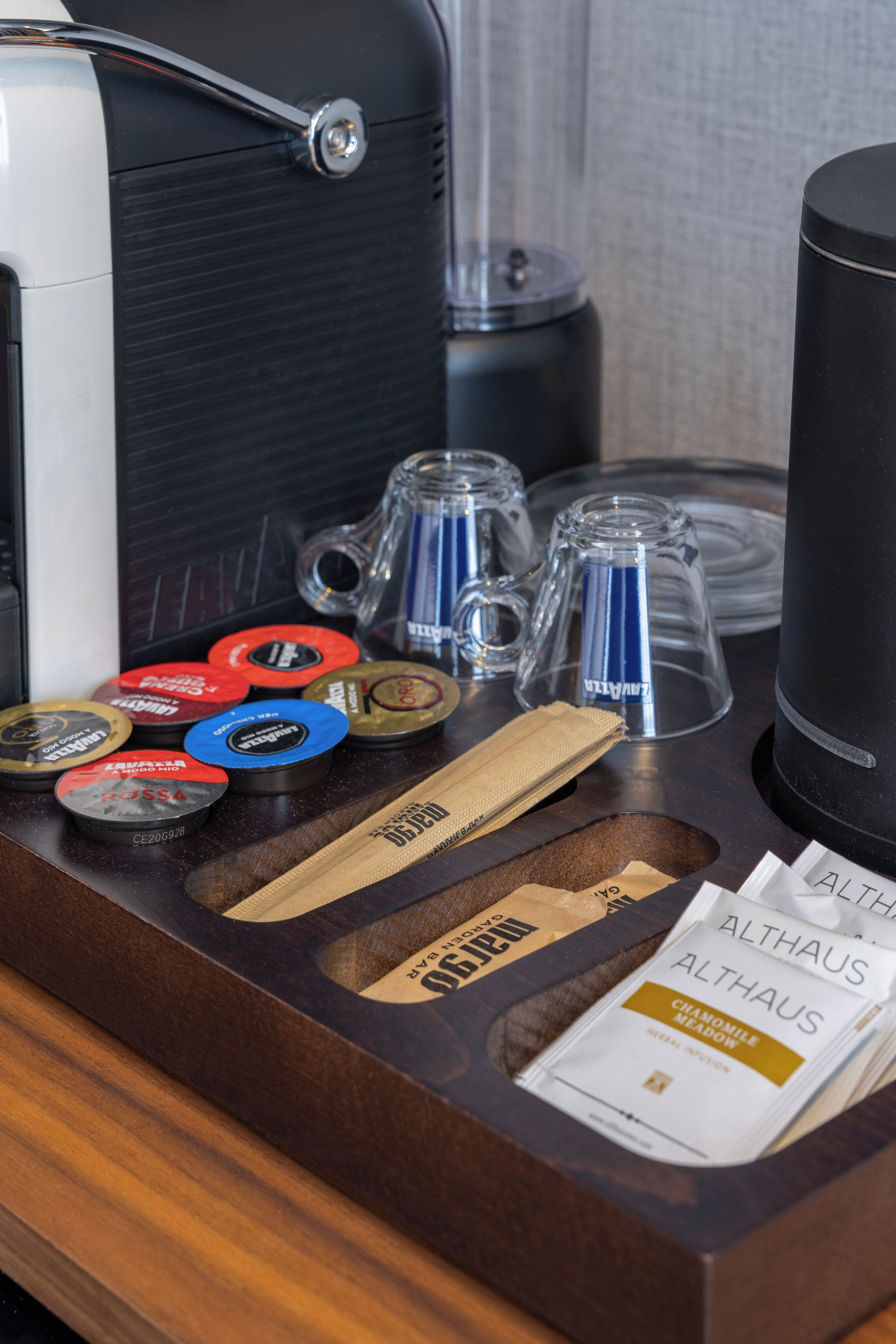A wooden tray with coffee mugs, a coffee maker, and various coffee pods.