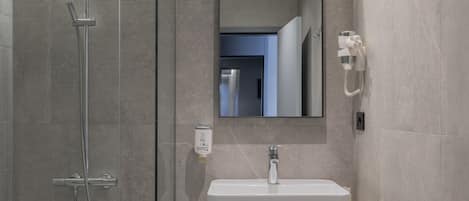 Un baño moderno con ducha envuelta en vidrio, un lavabo blanco y un mueble de tocador de madera.