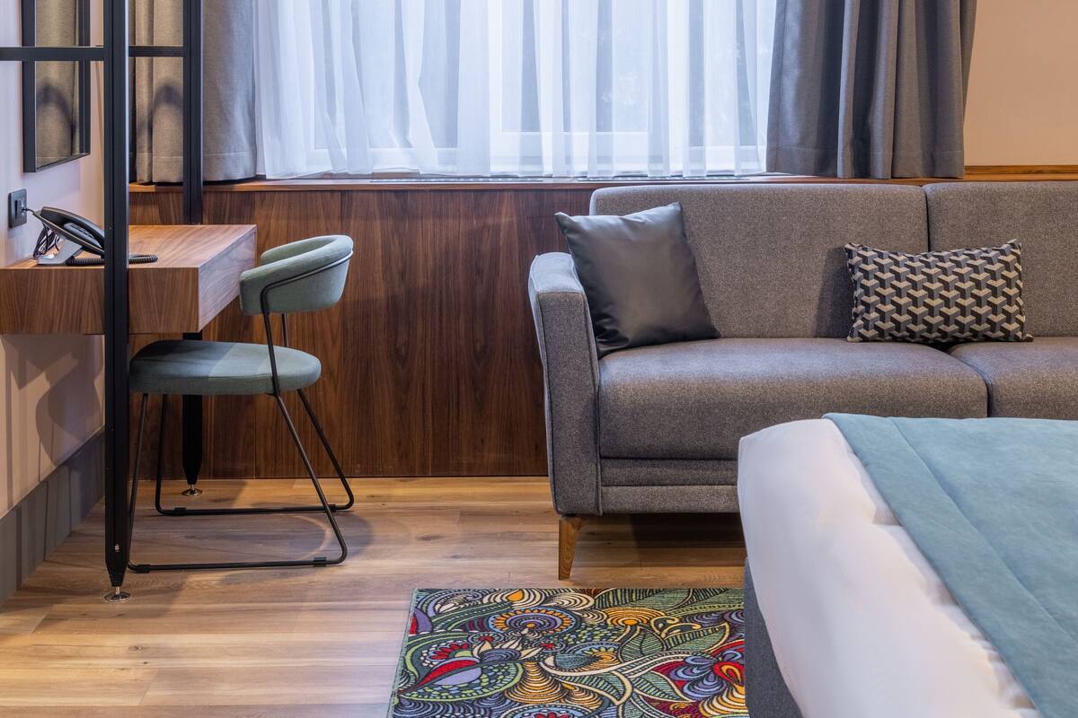 Una habitación de hotel moderna con un escritorio de madera, un sofá gris y una alfombra colorida.