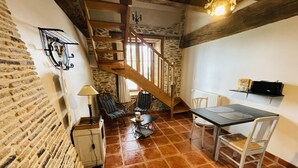 Un interior rústico con pared de piedra, una escalera de madera, una mesa de comedor con sillas y una lámpara.