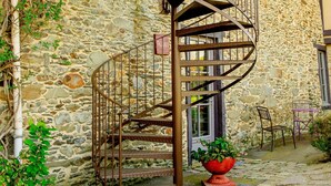 Un edificio de piedra con una escalera espiral que conduce a un balcón. Hay una maceta roja con plantas en el suelo.