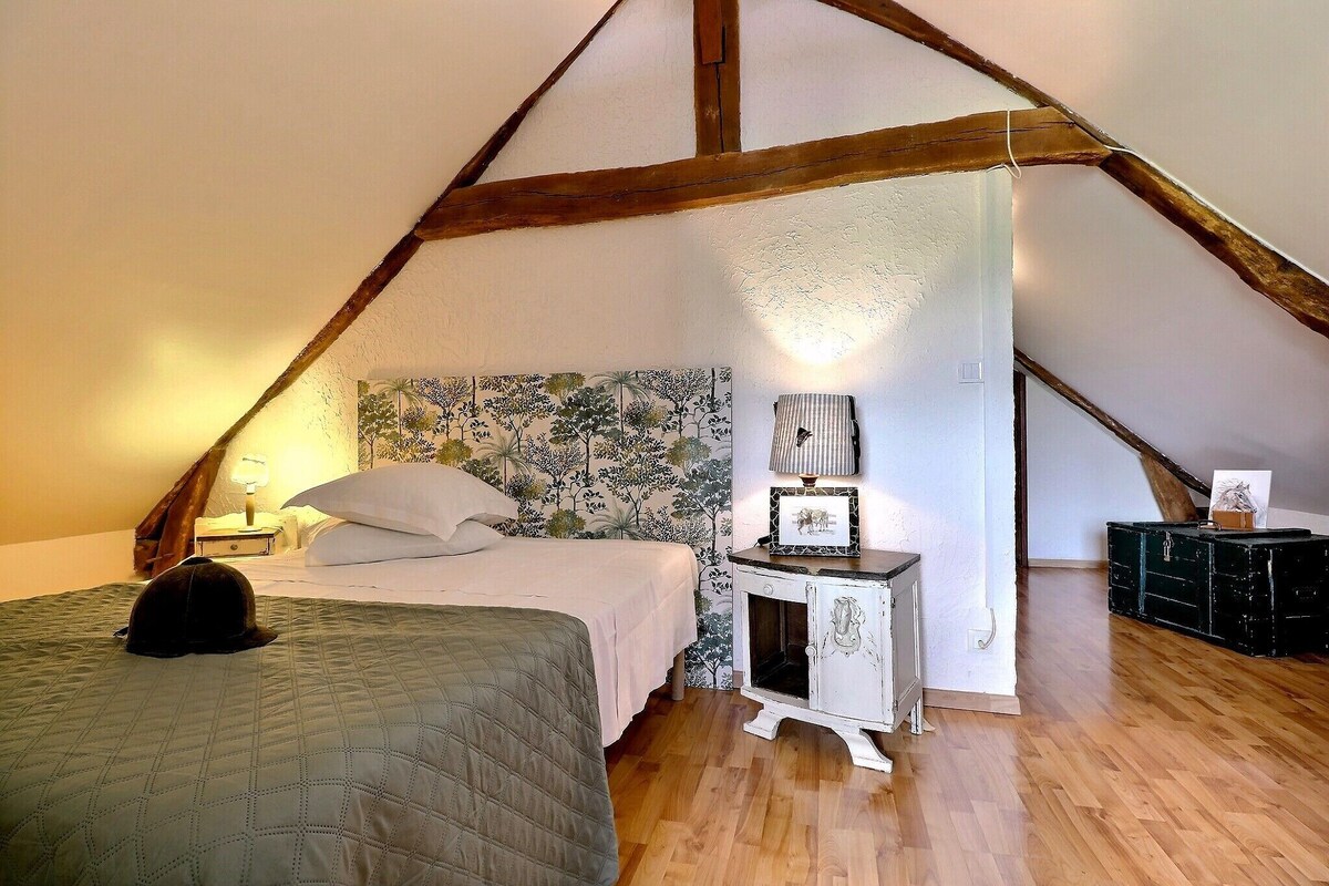 A bedroom with a sloped ceiling, a bed with a quilt, a nightstand with a lamp, and a dresser.
