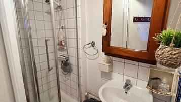 Ett badrum med en duschkabin med glasväggar, ett handfat på en piedestal och en spegel med träram.