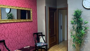 Un área de recepción con un banco de madera, dos sillas, un espejo, un reloj y una planta en maceta.