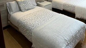 Habitación de hotel con dos camas, cada una con cabecero de madera, ropa de cama blanca y un muro decorado con un diseño de ramas de árbol. Hay mesitas de noche con lámparas.