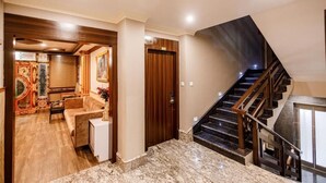 A spacious living area with a sofa and a coffee table, a wooden door, and a staircase with a dark railing. - Avana Lhayul (Gangtok)