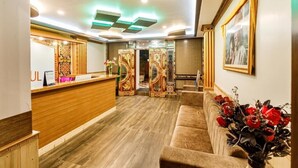 A reception area with a wooden reception desk, a sofa, and a wall with a framed picture. - Avana Lhayul (Gangtok)