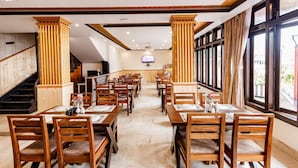 A restaurant with wooden tables and chairs, a TV screen, and large windows. - Avana Lhayul (Gangtok)