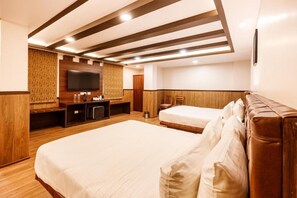 A hotel room with a large bed, a TV mounted on the wall, a wooden accent wall, and a ceiling with exposed beams. - Avana Lhayul (Gangtok)